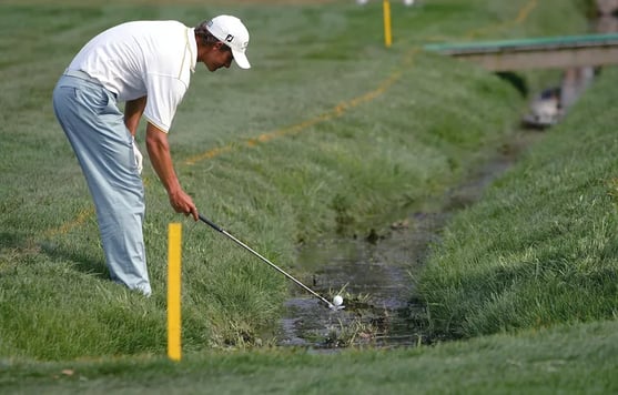 Yellow stakes indicate that Adam Scott is inside the boundary of a water hazard