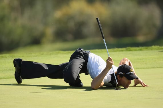 Camilo Villegas crouches close to the ground to line up a putt in a PGA Tour tournament.